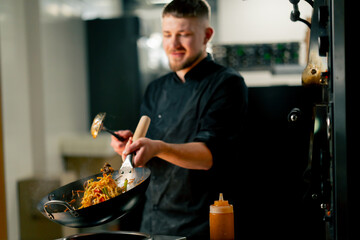 in professional kitchen the chef prepares wog noodles with vegetables on a large frying pan