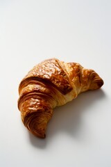 A single, freshly baked croissant rests on a white surface, its golden brown crust glistening under the light