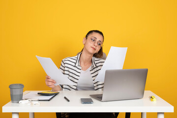Minded business woman, portrait of young caucasian brunette minded business woman sit office desk work with pc laptop hold paper account documents isolated yellow background. Career concept.