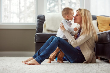 Home, fun and kiss of baby by mom, living room and playful with son, love and care in apartment. House, mother and toddler in lounge, hug and together on floor, happiness and wellness for boy