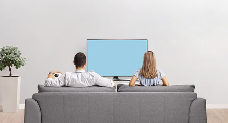 Rear view shot of a man holding a football sitting on a sofa with a woman and watching tv