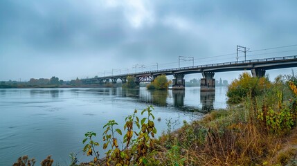 Fototapeta premium long bridge over wide river with a cloudy sky green vegetation as a background