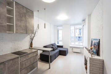 Spacious kitchen with minimalist square shaped furniture, grey floor and walls, counter with integrated sink and pair of bar stools in front of it, built-in microwave and cooktop. 