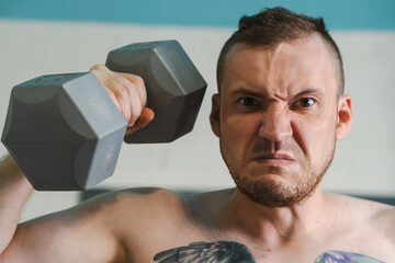 A shirtless man with a tattoo on his chest lifts a grey dumbbell