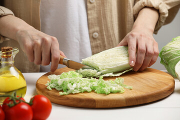 Woman cutting fresh chinese cabbage at white wooden table, closeup