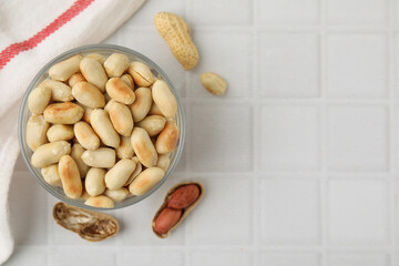 Roasted peanuts in bowl on white tiled table, top view. Space for text