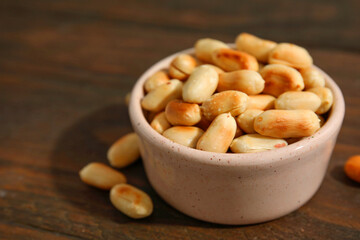 Roasted peanuts in bowl on wooden table, closeup. Space for text