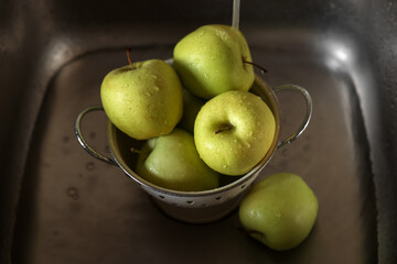 Washing fresh apples with tap water in metal colander inside sink