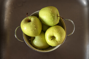 Fresh wet apples in metal colander inside sink, top view