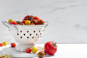 Metal colander with fresh tomatoes on white wooden table, space for text