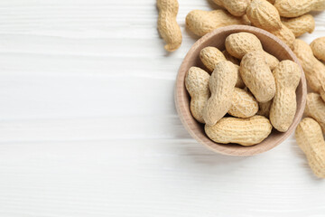 Fresh peanuts in bowl on white wooden table, top view. Space for text