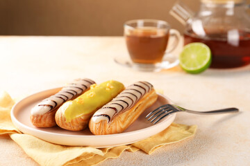 Different tasty glazed eclairs served on color textured table, closeup