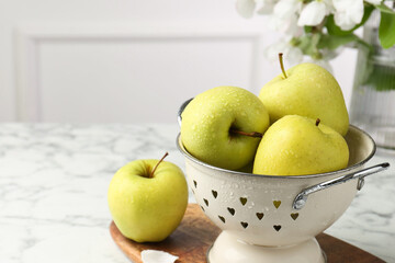 Colander with fresh apples on white marble table, space for text