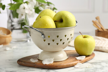 Colander with fresh apples and flower petals on white marble table