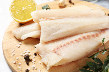 Pieces of raw cod fish, spices, parsley and lemon on table, closeup