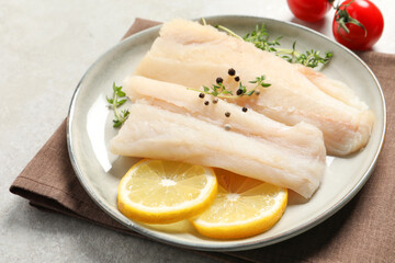 Plate with raw cod fish, spices, microgreens and lemon on grey table, closeup