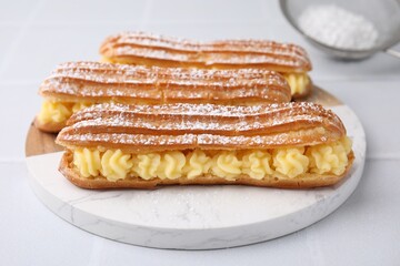 Delicious eclairs filled with cream on white table