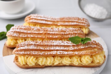 Delicious eclairs filled with cream and mint on table, closeup