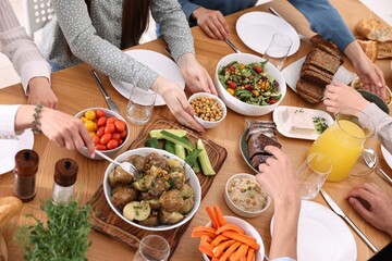 Friends eating vegetarian food at wooden table indoors, closeup