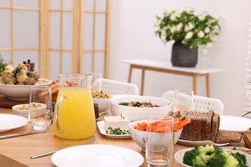 Healthy vegetarian food, jug of juice, cutlery, glasses and plates on wooden table indoors