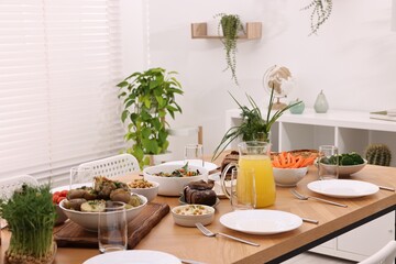 Healthy vegetarian food, jug of juice, cutlery, glasses and plates on wooden table indoors