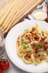 Tasty pasta with bacon and basil on white marble table