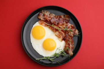 Fried eggs, bacon and microgreens on red background, top view