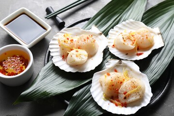 Raw scallops with spices, lemon zest, shells and sauces on grey textured table, closeup
