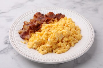 Delicious scrambled eggs with bacon in plate on white marble table