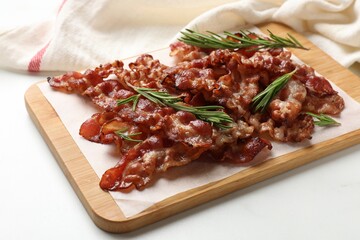 Slices of tasty fried bacon with rosemary on white table