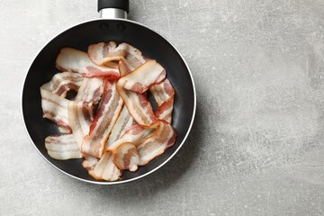 Delicious bacon slices in frying pan on light grey table, top view. Space for text