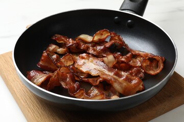 Delicious bacon slices in frying pan on white table, closeup