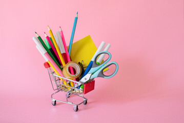 School and office supplies in shopping cart on pink background