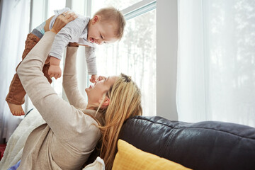Fototapeta premium Couch, playing and baby with mom, lounge and bonding with son, morning and love in apartment. Home, mother and toddler in living room, laughing and together on sofa, happiness and care for boy
