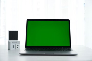 computer with a green screen on a white background.
Laptop stands on a white table