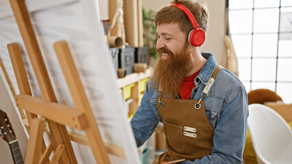 Handsome, young, redhead bearded man, joyfully engrossed in a painting lesson, listening to...