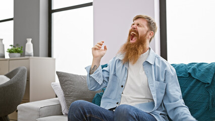 Troubled young redhead man, alone indoors, stress screaming on the sofa