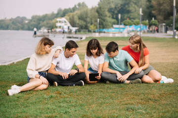 Summer holidays and teenage concept - group of smiling teenagers with tablet hanging out outside.