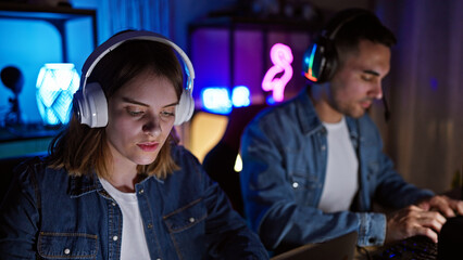 A man and woman in headphones focused on gaming in a neon-lit room at night. © Krakenimages.com