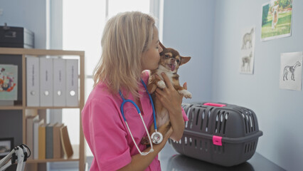A young blonde woman veterinary in a clinic, wearing a pink uniform and stethoscope, lovingly...
