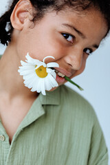 Innocence captured young boy holds a delicate white flower in his mouth, gazing confidently at the...