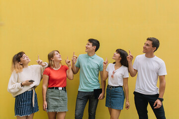 Happy group teenagers show something on the yellow background with copy space.