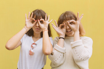 Two stylish school friends girl joking and make faces grimace with hands on the yellow background