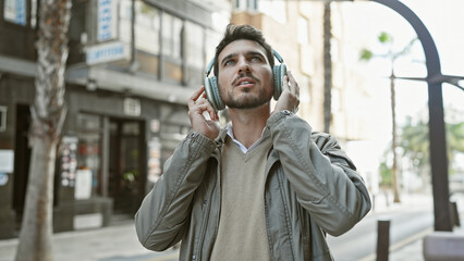Fototapeta premium Handsome hispanic man with beard wearing headphones in an urban city street.