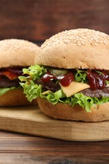 Board with delicious cheeseburgers on wooden table, closeup