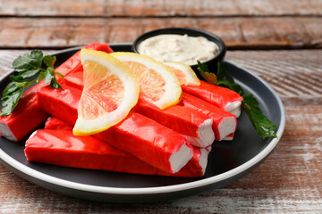 Tasty crab sticks, sauce, pieces of lemon and parsley on wooden table, closeup