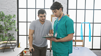 Fototapeta premium A male physiotherapist consulting with a male patient in an indoor rehabilitation clinic.