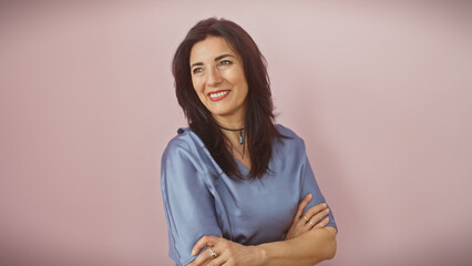 Fototapeta premium Mature hispanic woman with crossed arms smiling against a pink background