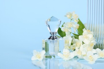 Aromatic perfume in bottle and beautiful jasmine flowers on light blue background, closeup. Space...