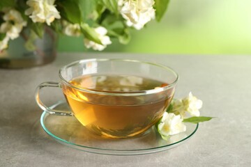 Aromatic jasmine tea in cup, flowers and green leaves on light grey table